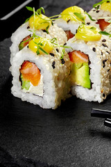 Uramaki sushi rolls with salmon, avocado, cream cheese, mango sauce and sesame seeds on black stone...