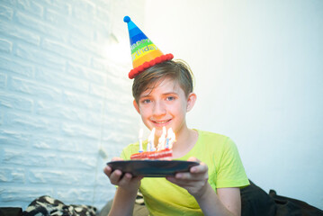Happy little adorable boy celebrates his birthday. The boy looks at a piece of cake with candles,...