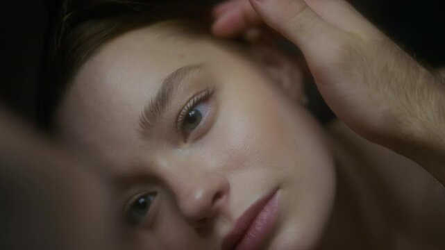 Extreme close-up shot of young ethereal woman with blue eyes and plump lips looking with love at her spouse who stroking her gently over face, intimacy and warmth