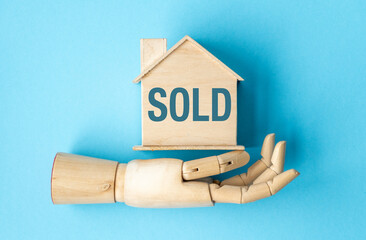 A wooden hand holding a house that says Sold on it