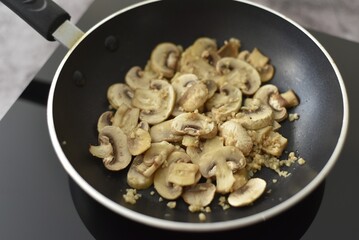 A pan full of fried mushrooms with chopped garlic on an induction hob.