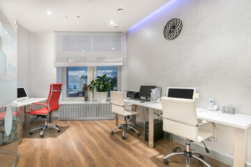 A cozy office with a white interior. A desk with office equipment, comfortable chairs.