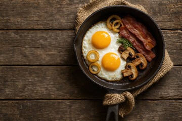 Delicious rustic breakfast of fried eggs, bacon, mushrooms, and onion rings in a cast iron pan on a wooden table. Traditional morning meal with fresh ingredients and country-style setting.