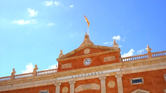 Waving catalan flag blowing in wind against historic tarragona city hall facade under bright blue sky with white clouds on sunny day