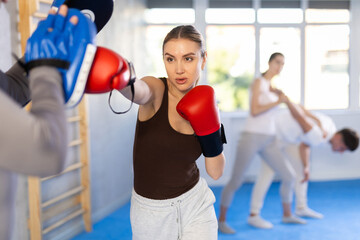 Active young girl training boxing kicks on punch mitts held by instructor in sports hall