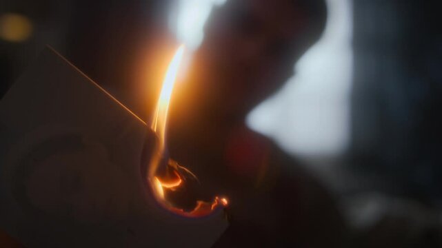 Close-up low key shot of melancholic man with sorrow in heart looking sadly at burning photo of beloved ex-girlfriend, painful breakup
