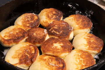 Golden brown pieces of fried dough sizzle in a black skillet, glistening with oil.