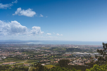 Panoramic view from Santa Eufémia in Sintra, Portugal, capturing the vast coastal landscape with blue skies, urban areas, and the Atlantic Ocean on a clear sunny day.