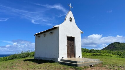 Saint Peter Chapel, a tiny whitewashed chapel built by fisherman on the top of a mound. Blue sky, white clouds, green lawn. Fernando de Noronha island, Brazil. Sunny day, beautiful view. Cirrus clouds