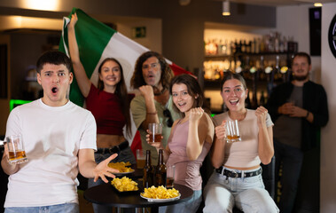 Group of friends fans watching match cheering with Italian flag in bar
