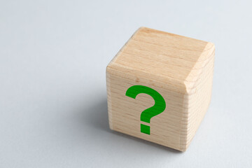Wooden cube with green question mark on light grey background, closeup