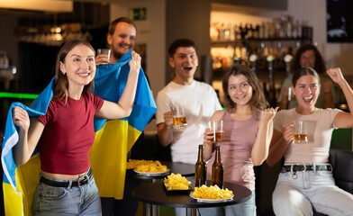 Group of fans of Ukrainian team with a flag are watching the match on TV in a beer bar. They are worried and supporting their favorite team
