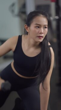 Focused asian woman performing bent-over dumbbell row workout at gym, wearing black sportswear, showcasing strength, fitness, and healthy lifestyle in action