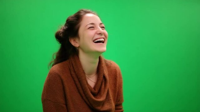 Joyful Laughter Against Green Backdrop: Capturing a moment of pure happiness and amusement, a young woman erupts in spontaneous laughter against a vivid green background.