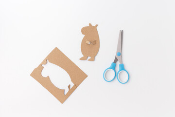 Cardboard capybara figure cut out with blue scissors on white background. DIY crafting process. Studio photo. Kids handmade art project and creative activity. part of project