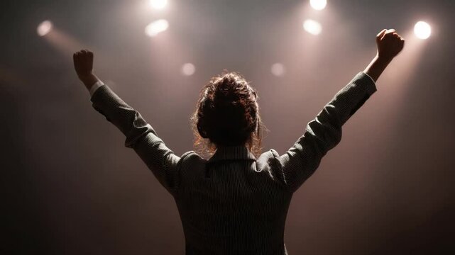 Triumphant Speaker: A woman celebrates her success on stage, arms raised in victory, silhouetted against bright spotlights. The image evokes feelings of empowerment and accomplishment.