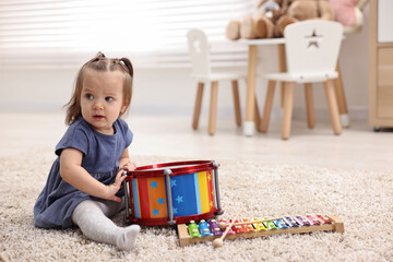 Naklejka premium Cute little girl playing with toy drum on floor at home, space for text