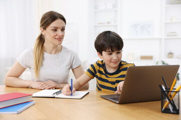 Obraz premium Mother helping her son with homework at wooden table indoors