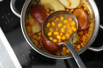 Taking tasty compot with ladle from pot on stove, top view
