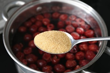 Adding sugar into tasty cherry compot in pot on stove, closeup