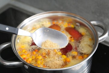 Adding sugar into tasty compot in pot on stove, closeup