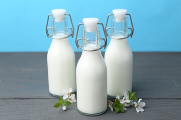 Fresh milk and blossoms on wooden table against light blue background
