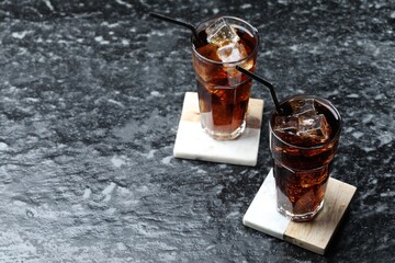 Refreshing cola with ice cubes and straws in glasses on dark textured table. Space for text
