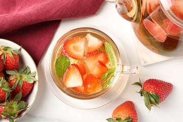 Aromatic fruit tea with strawberries and mint on white marble table, flat lay