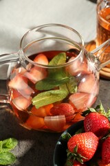 Glass teapot with aromatic fruit tea, strawberries and mint on grey table, closeup