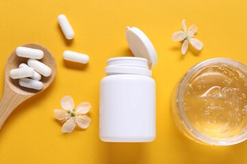 Collagen capsules, gel and flowers on orange background, flat lay
