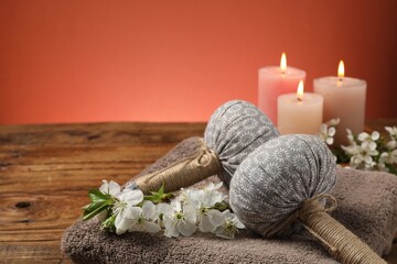Spa composition with herbal bags, beautiful flowers and burning candles on wooden table against coral background, closeup. Space for text