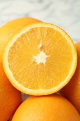 Half of fresh orange among whole ones on blurred light background, closeup