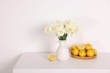 Beautiful daffodils in vase and lemons on white wooden table. Space for text