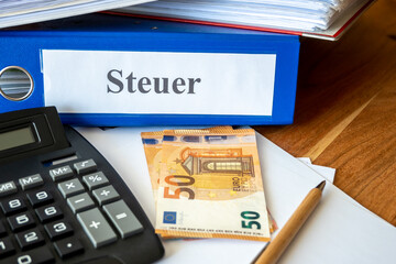 Blue, red folders with tax paper, money bills, pen and calculator on the table.
