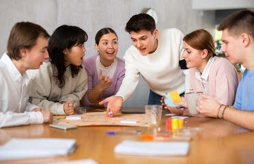 Happy carefree student playing board game with group of friends at table in campus. Concept of leisure and communication of young people