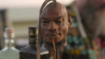 Close-up footage of a shrunken head decoration in the foreground, set at an outdoor bar. In the softly blurred background, a bartender prepares tropical cocktails, adding atmosphere and depth.