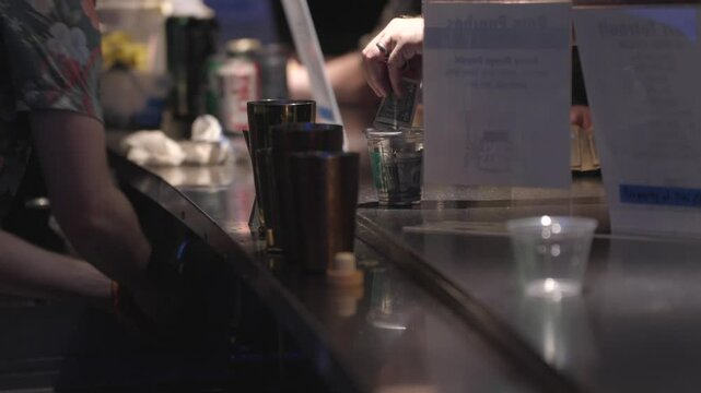 Evening footage inside a bustling bar, capturing a customer placing cash into a tip jar.