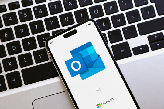 Mobile phone over a laptop keyboard opening Outlook app for mail of Microsoft. ROSARIO, ARGENTINA - APRIL 30, 2025.