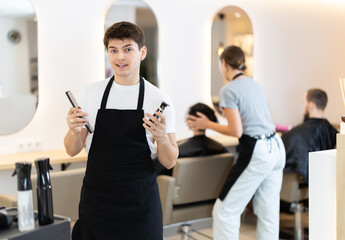 Young guy hairdresser stylist posing with comb and electric razor in beauty salon