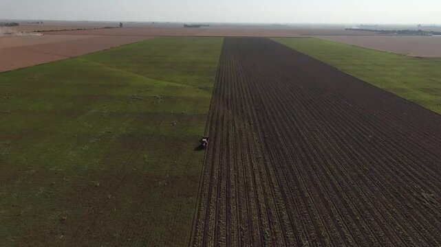 A&eacute;rea de campo argentino, tractor con rastrillo arrancando man&iacute;, toma de dron, tierra en el aire