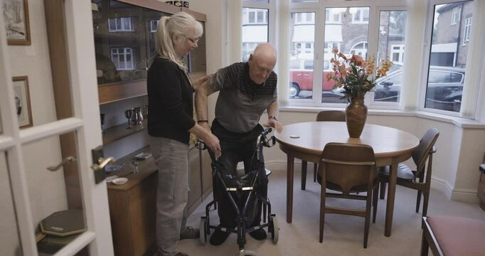 Walker, old woman help senior man and physiotherapy for recovery, healthcare and disability in nursing home. Love, male elderly citizen and mature female assist husband, living room and retirement