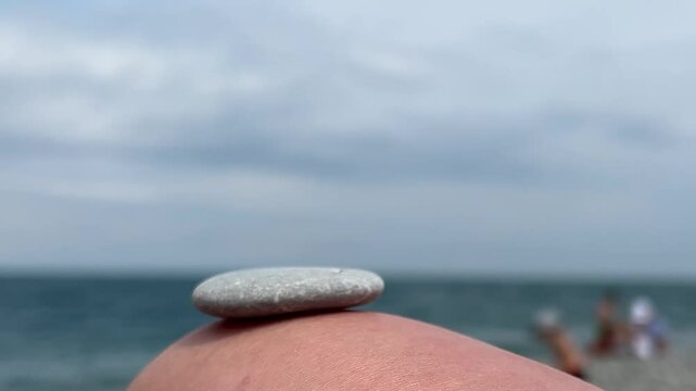 Horizontal video 4K close up. Male hand builds small rock tower on female knee. Blue sky. Light stones. Sun, sea waves, coastline. Rest on pebble beach, calm, yoga, travel, ocean shore zen, tourism