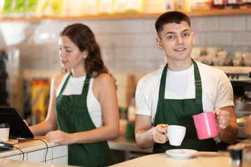 Man and a woman barista prepare a cappuccino and add milk to it. Coffee shop workers prepare an...