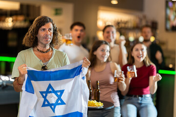 Group of fans watch match and cheer with Israeli flag in pub