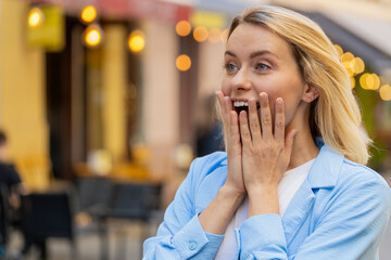 Oh my God, wow. Caucasian young woman looking surprised at side with big open eyes shocked by sudden victory, game winning, lottery goal achievement, good news outdoors. Lady on city sunshine street