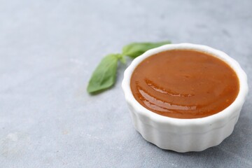 Tasty curry sauce and basil leaves on grey table, closeup. Space for text