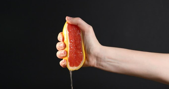 Woman squeezing grapefruit on black background, closeup. Space for text
