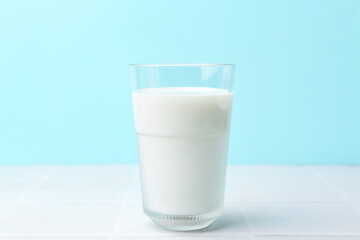 Glass of fresh milk on white tiled table against light blue background