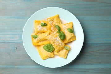 Delicious ravioli with cheese and basil on light blue wooden table, top view