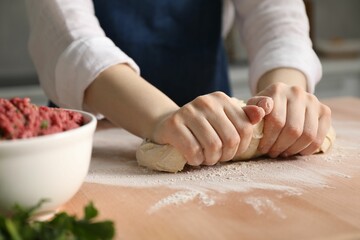 Making khinkali. Woman kneading dough at table in kitchen, closeup
